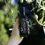 Main tenant l'huile d'olive bio Racilia 100 ml entre les branches d'olivier avec des olives